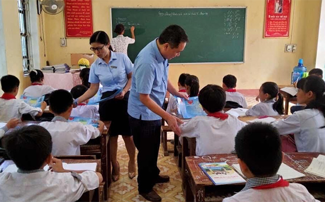 Cán bộ Bảo hiểm xã hội huyện Yên Bình phát tờ rơi tuyên truyền chính sách BHYT tại Trường Tiểu học và THCS xã Hán Đà.