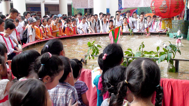 Đông đảo học sinh chăm chú xem tiết mục rối nước của phường rối Đào Thục, Đông Anh, Hà Nội trong ngày hội.