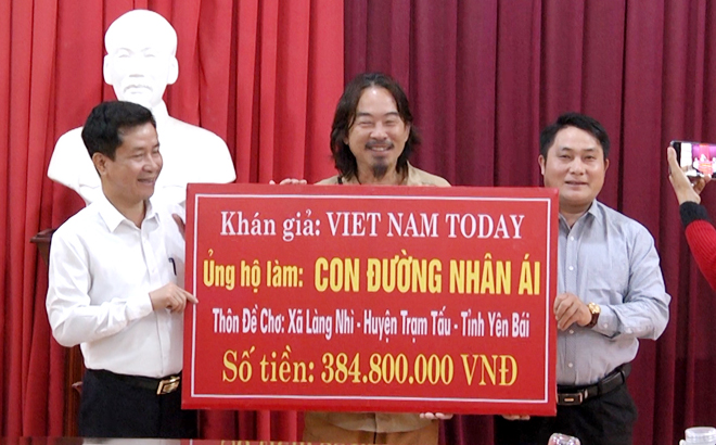 Journalist Truong Nguyen (C), owner of the Vietnam Today YouTube channel, presents the token of the donation for building the concreate road in De Cho.