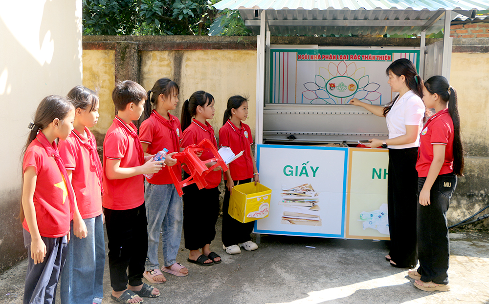 Học sinh Trường Tiểu học Sơn Thịnh nghe cô giáo Tổng phụ trách Đội của nhà trường hướng dẫn phân loại rác và bỏ vào ngăn theo đúng hướng dẫn tại 