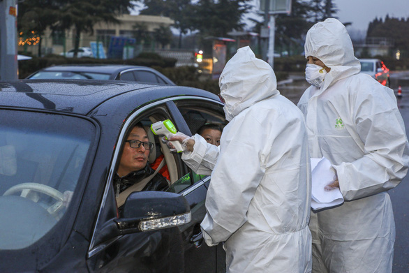 Các nhân viên y tế mang thiết bị bảo hộ kiểm tra thân nhiệt của một tài xế tại điểm kiểm tra trên đường cao tốc ở thành phố Đằng Châu, tỉnh Sơn Đông hôm 26/1