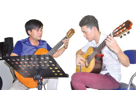 Nhà giáo, nhạc sĩ Bùi Quốc Huy (trái) hướng dẫn học trò chơi đàn ghi - ta.