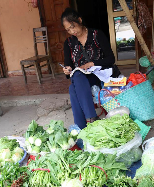Chị Trần Thị Hợp say mê viết sách bên sạp rau bán vỉa hè.