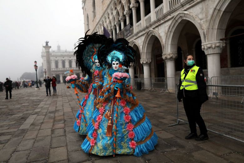 Một nữ cảnh sát đeo mặt nạ đứng cạnh những người vui chơi lễ hội tại Venice Carnival, ngày 23/2.
