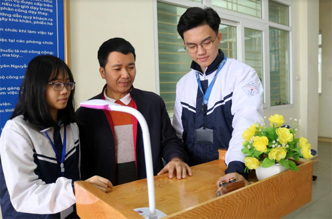 Thầy giáo Đặng Tiến Thành (đứng giữa) cùng các em Vũ Mai Hồng và Nguyễn Đức Chiến giới thiệu sáng chế bục phát biểu thông minh.