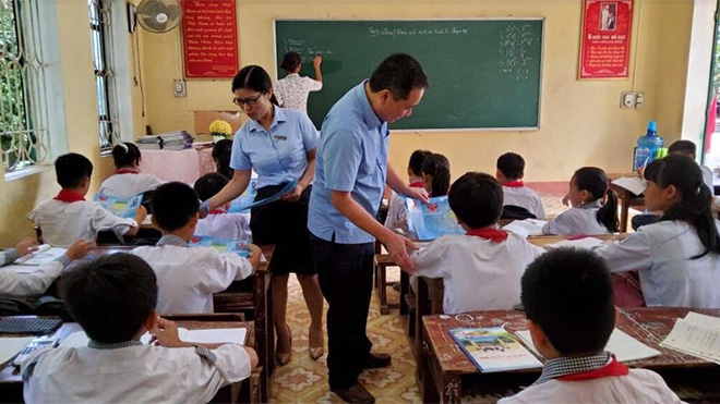 Cán bộ Bảo hiểm xã hội huyện Yên Bình phát tờ rơi tuyên truyền chính sách bảo hiểm y tế học sinh, sinh viên tại các trường học trên địa bàn huyện.