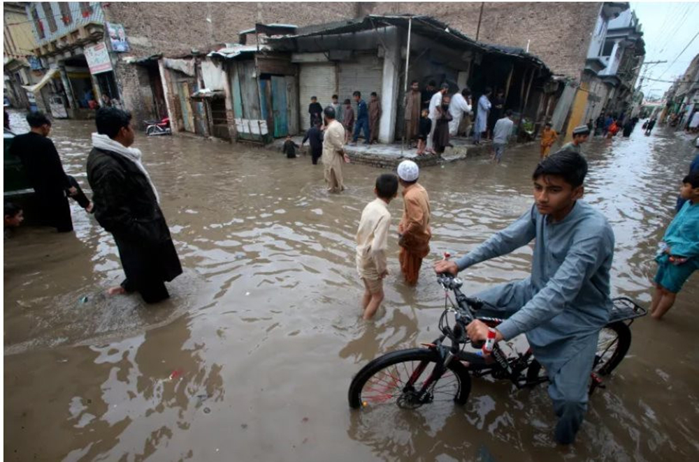 Trẻ em lội qua đường phố ngập nước do mưa lớn ở Peshawar, Pakistan, ngày 15-4. Ảnh: Muhammad Sajjad
