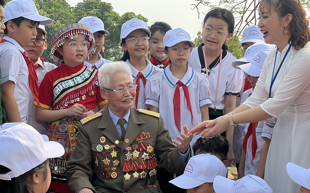 Cựu chiến sĩ Điện Biên Phạm Đức Cư chia sẻ những câu chuyện thời chiến với các em học sinh và phóng viên tại Di tích Đồi A1.
