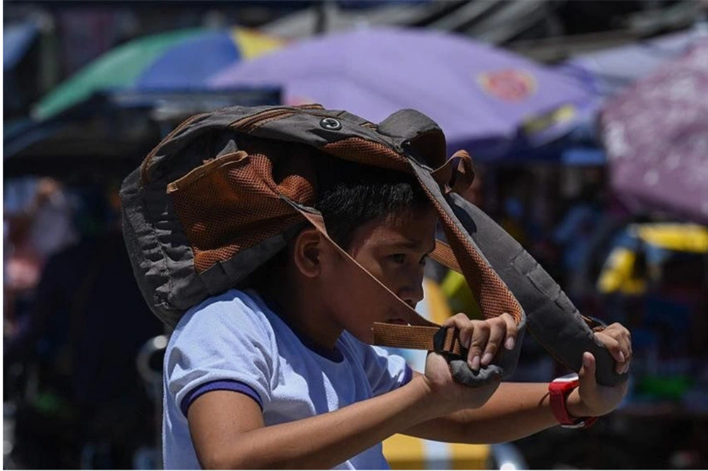 Một học sinh tại Manila lấy cặp để che đầu khi đến trường dưới thời tiết nắng nóng