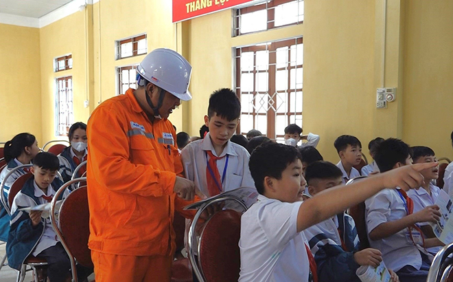 Cán bộ Điện lực Văn Yên tuyên truyền đến các em học sinh các quy định về bảo vệ an toàn đường dây dẫn điện trên cao và hành lang bảo vệ an toàn công trình điện trên tờ rơi.