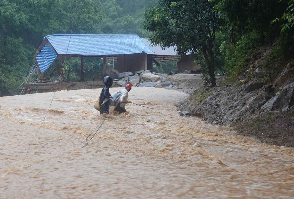 Người dân xã Hồ Bốn, huyện Mù Cang Chải cố gắng vượt qua dòng nước lũ để di chuyển đến nơi an toàn trong trận lũ lịch sử ngày 5/8/2023. (Ảnh: TTXVN)