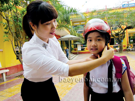 Giáo viên Trường Tiểu học Nguyễn Trãi (thành phố Yên Bái) hướng dẫn học sinh cách đội mũ bảo hiểm.
