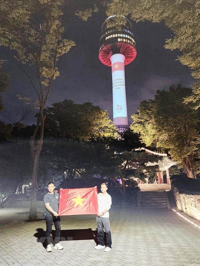 Hai thanh niên Việt Nam tại Hàn Quốc tự hào chụp ảnh bên lá quốc kỳ dưới chân tháp Namsan.