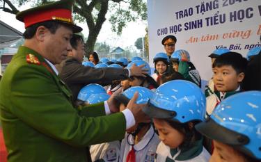 Lãnh đạo Ban An toàn giao thông tỉnh hướng dẫn học sinh Trường Tiểu học Mậu A, huyện Văn Yên đội mũ bảo hiểm đúng cách. (Ảnh: Thanh Chi)