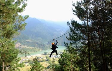 Một nam du khách vừa trượt zipline vừa cầm điện thoại quay chụp.