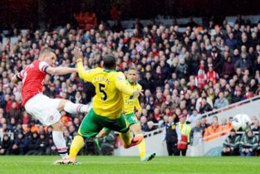 Tiền đạo Podolski tung cú sút ghi bàn vào lưới Norwich ấn định chiến thắng 3 - 1 cho Arsenal.