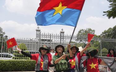 Người dân vẫy cờ Mặt trận Dân tộc Giải phóng miền Nam khi chụp ảnh trước Dinh Độc Lập ngày 29/4.