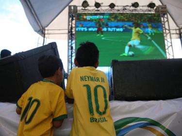 Hai cổ động viên nhí xem đội tuyển Brazil thi đấu với Cameroon trên màn hình lớn.