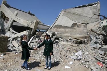 Hai bé gái đứng trước ngôi trường bị phá hủy hoàn toàn do xung đột ở dải Gaza.