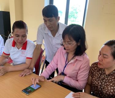 Cán bộ NHCSXH Chi nhánh tỉnh Yên Bái tuyên truyền, hướng dẫn người dân sử dụng ứng dụng VBSP Smart Banking tại điểm giao dịch xã.
